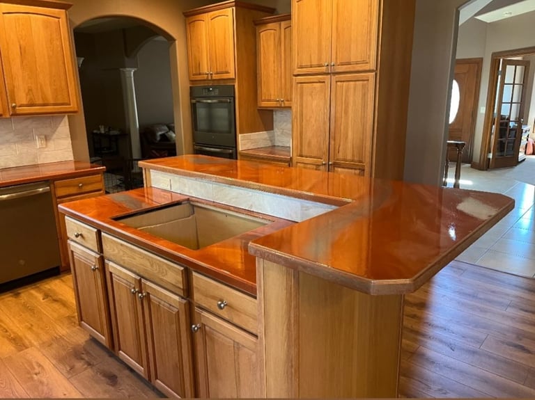 Luxury kitchen with wooden island featuring red granite countertop and sink, wooden cabinetry, and stainless steel appliances