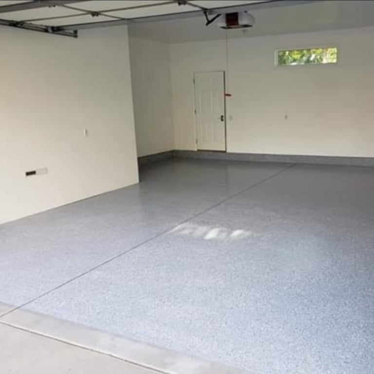 Empty garage interior with gray epoxy flooring, white walls, overhead door, and small window