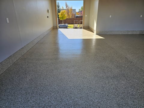 Empty garage interior with polished concrete floor and open door overlooking residential neighborhood