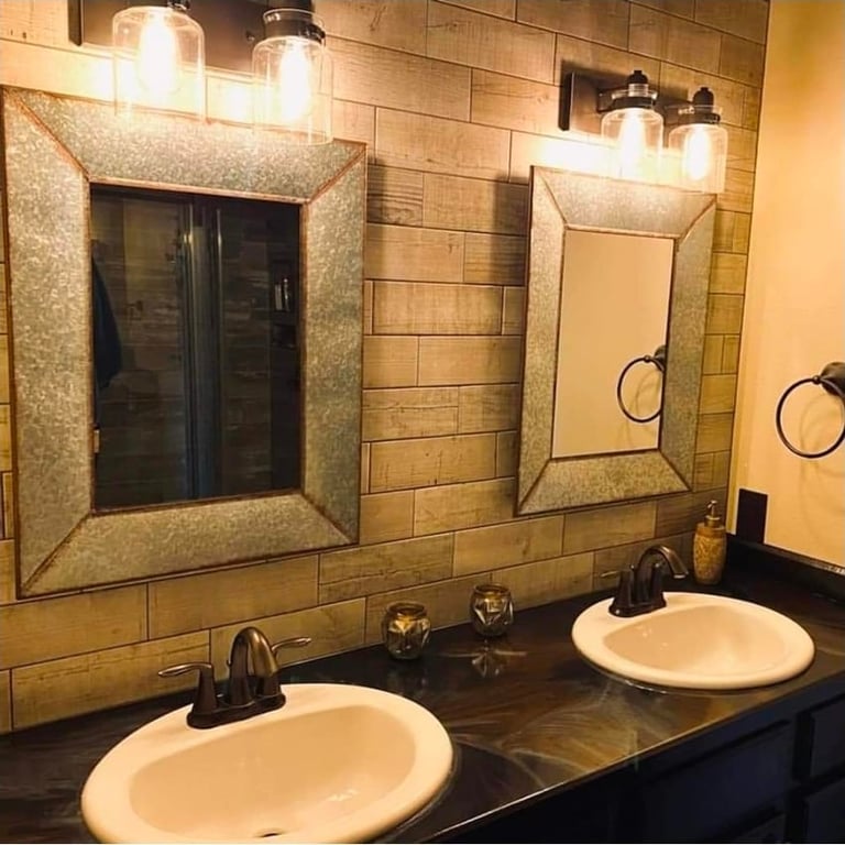 Modern bathroom vanity with dual white sinks, black faucets, decorative mirrors with gold frames, and warm lighting from wall sconces