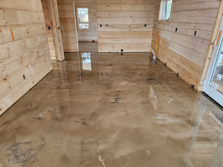 Interior of a wooden cabin or house with exposed stud walls, concrete flooring, and window openings during construction