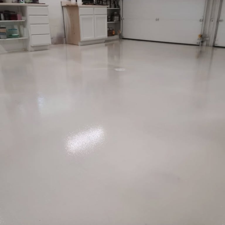 Spacious garage interior with shiny white epoxy flooring, white storage cabinets, and white garage door in background