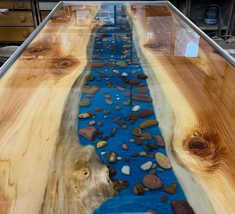 Epoxy resin river table with blue resin and decorative stones between natural wood planks