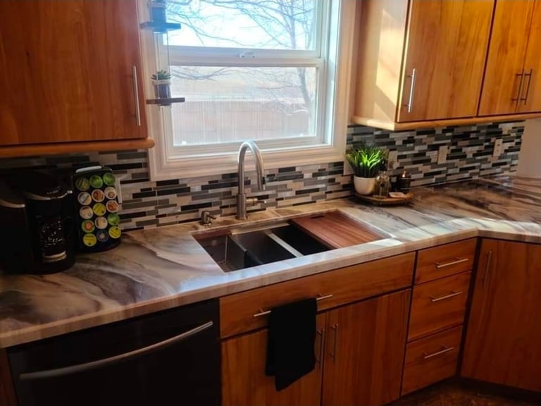 Modern kitchen with wood cabinets, marble countertop, black tile backsplash, stainless steel sink, and window overlooking snowy landscape