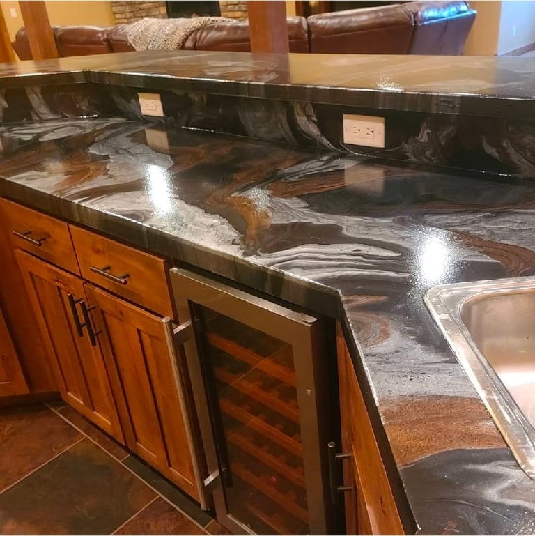 Modern kitchen island with dark marbled countertop, wood cabinetry, stainless steel sink, and wine cooler with living room visible in background