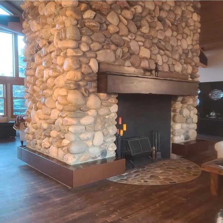 Large stone fireplace with rounded river rocks in a modern interior with wooden flooring and a hearth