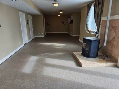 Empty basement room with beige carpet, white closet doors, window with curtains, and blue trash can