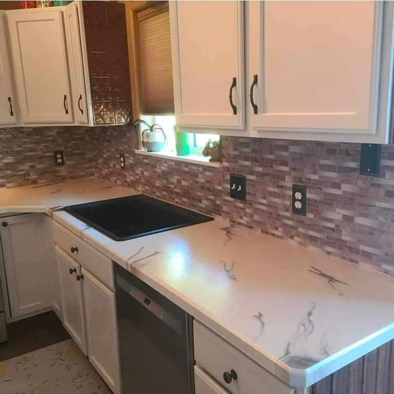 Modern kitchen with white cabinetry, white marble countertops, black cooktop, and brown brick backsplash
