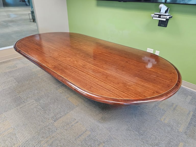 Large oval wooden conference table with polished cherry finish in a modern office with green wall