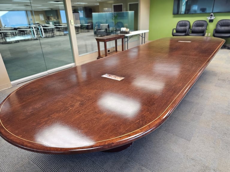 Large wooden conference table in a modern office boardroom with glass walls and green accent wall
