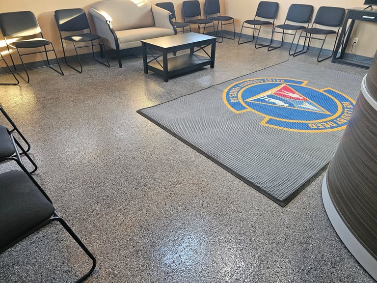 Interior of an official meeting room with blue and gold emblem floor mat, metal chairs, and casual seating arrangement